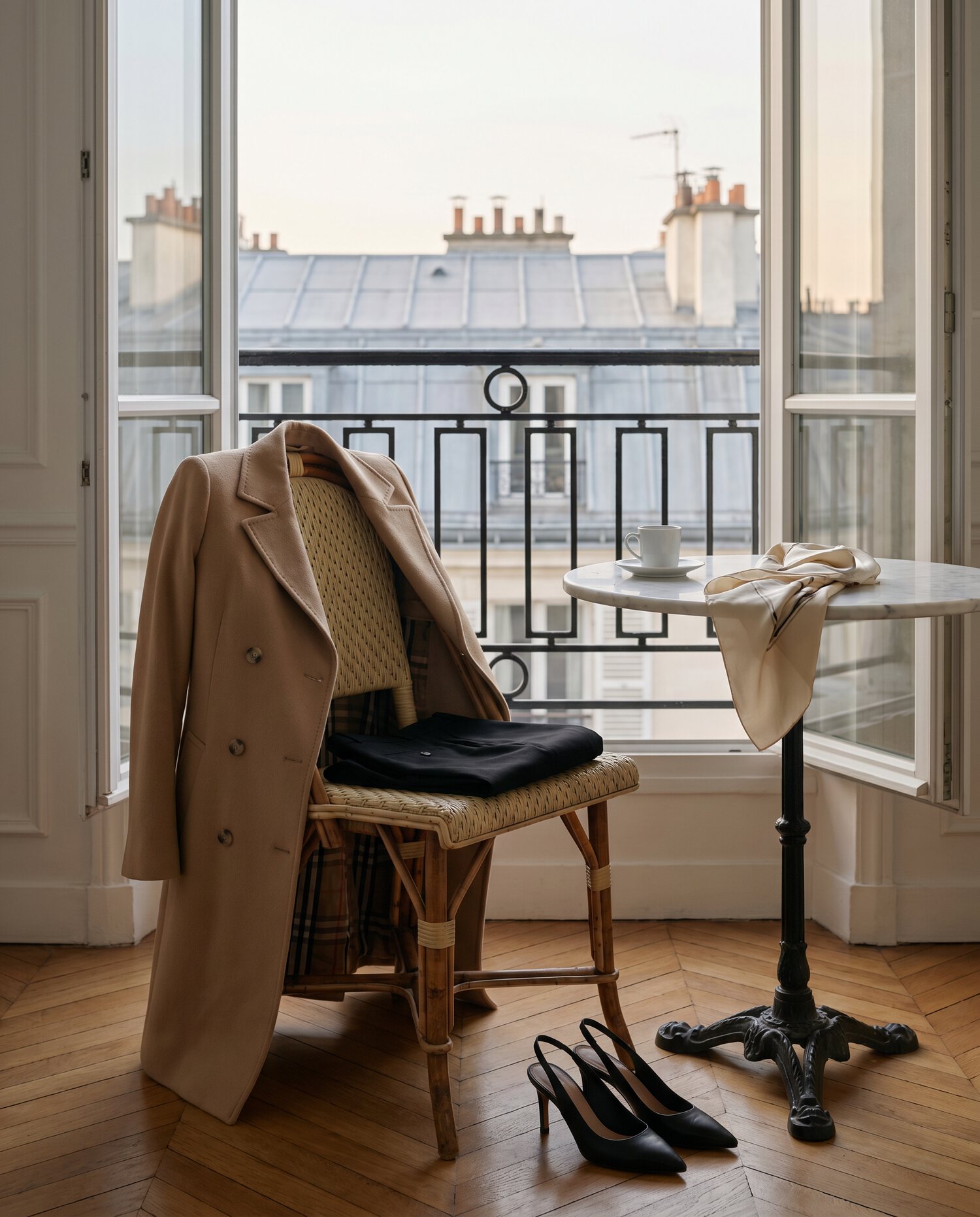 Camel trench over a bistro chair, Paris rooftops beyond